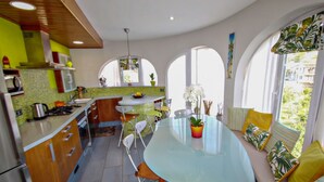 Une cuisine avec une table à manger en verre, des chaises blanches et une vue sur la verdure à l’extérieur.
