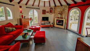 Un salon spacieux avec un plafond haut, des poutres apparentes, une cheminée, un téléviseur et de grandes fenêtres.