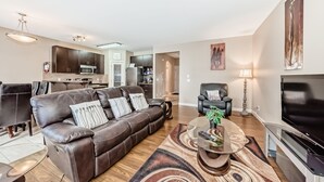 A modern living room with a brown leather sofa, a glass coffee table, a TV, and a dining area with a table and chairs. - Rome, Sweet Home. 

Spacious 4 Bedroom Single detached house - 60 mins to Banff. (Calgary)
