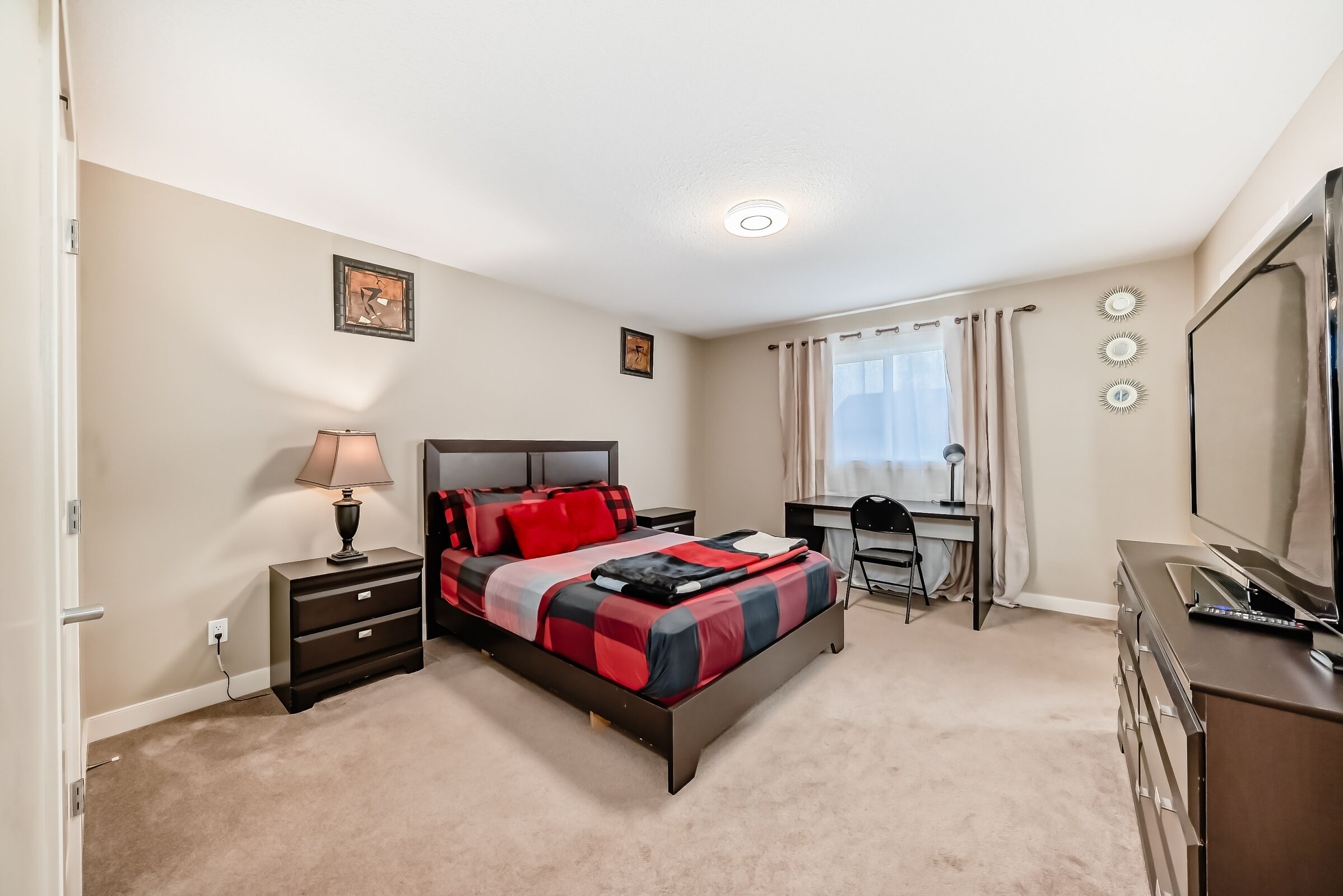 A bedroom with a bed, bedside table, lamp, desk, chair, and a dresser.