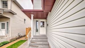 A residential building with a front porch, a set of concrete steps leading to a white door, and a small garden area with a wooden fence. - Rome, Sweet Home. 

Spacious 4 Bedroom Single detached house - 60 mins to Banff. (Calgary)