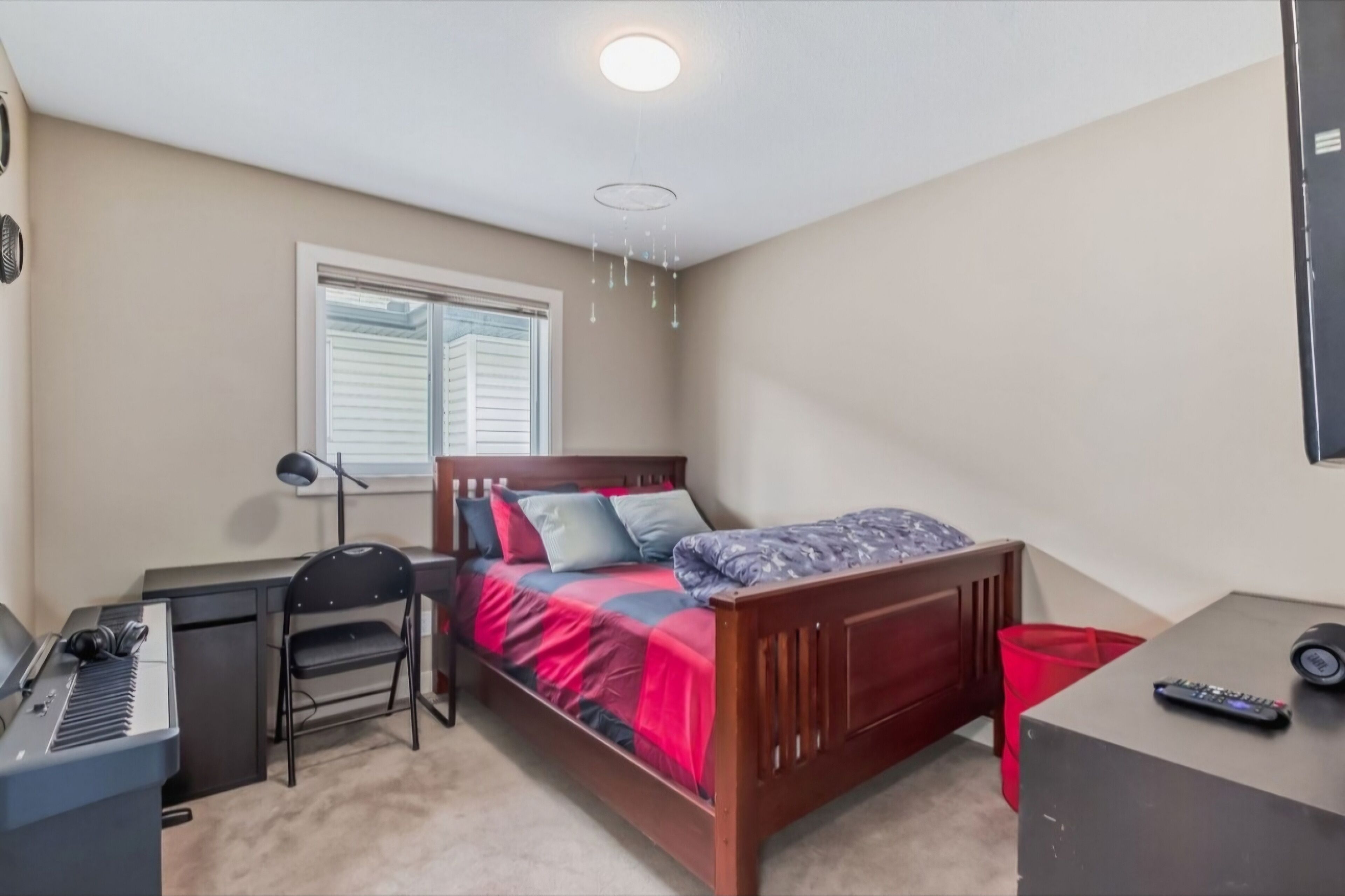A bedroom with a bed, a desk with a keyboard, a chair, a lamp, and a window.