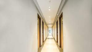 A long, narrow hotel corridor with doors on both sides, recessed lighting on the ceiling, and a tiled floor. - Hotel The Reef (Mohali)