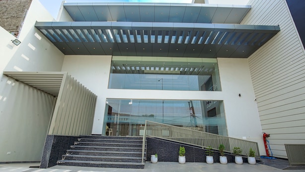 A modern building with a glass facade, a staircase leading to the entrance, and potted plants at the base. - Hotel The Reef (Mohali)