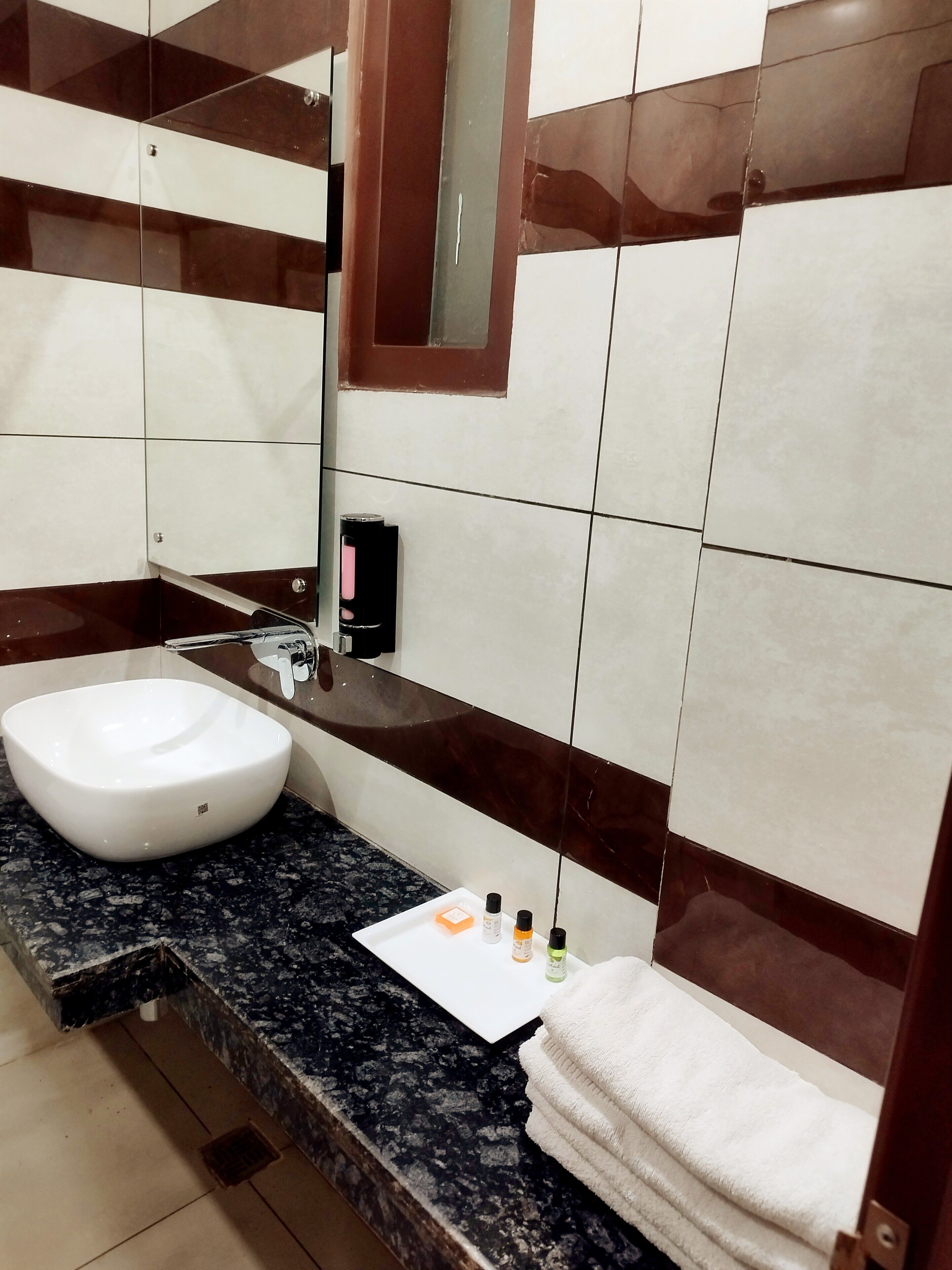 A bathroom with a white sink, dark granite countertop, and a mirror above it. There are toiletries on the counter and a towel hanging on the wall.