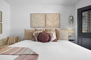 Une chambre à coucher avec un lit, des oreillers, une table de chevet et des œuvres d’art murales.
