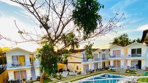 A resort with multiple-story buildings, a swimming pool, and a tree-lined courtyard. - Tvessa A Boutique Hotel Goa (Ashvem)