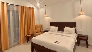 A modern bedroom with a large bed, two bedside tables, a chair, and a ceiling fan. - Tvessa A Boutique Hotel Goa (Ashvem)