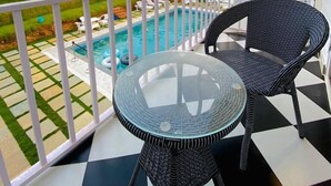 A balcony with a checkered floor, two wicker chairs, a glass table, and a pool in the background. - Tvessa A Boutique Hotel Goa (Ashvem)