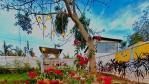 A garden with a white planter, red flowers, and a tree. - Tvessa A Boutique Hotel Goa (Ashvem)