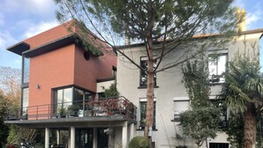 Ein modernes Gebäude mit roter Backsteinfassade, einem Balkon mit Blumentöpfen und einer Schotterauffahrt.