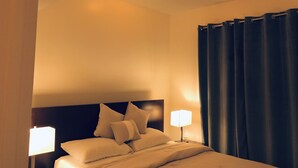 Una camera d'albergo con un letto, due lampade da comodino, una testiera e una tenda.