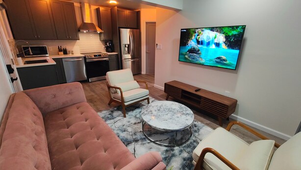 Una cucina moderna con elettrodomestici in acciaio inossidabile, una TV a schermo piatto fissata al muro, un divano rosa in velluto e un tavolino da caffè in marmo.