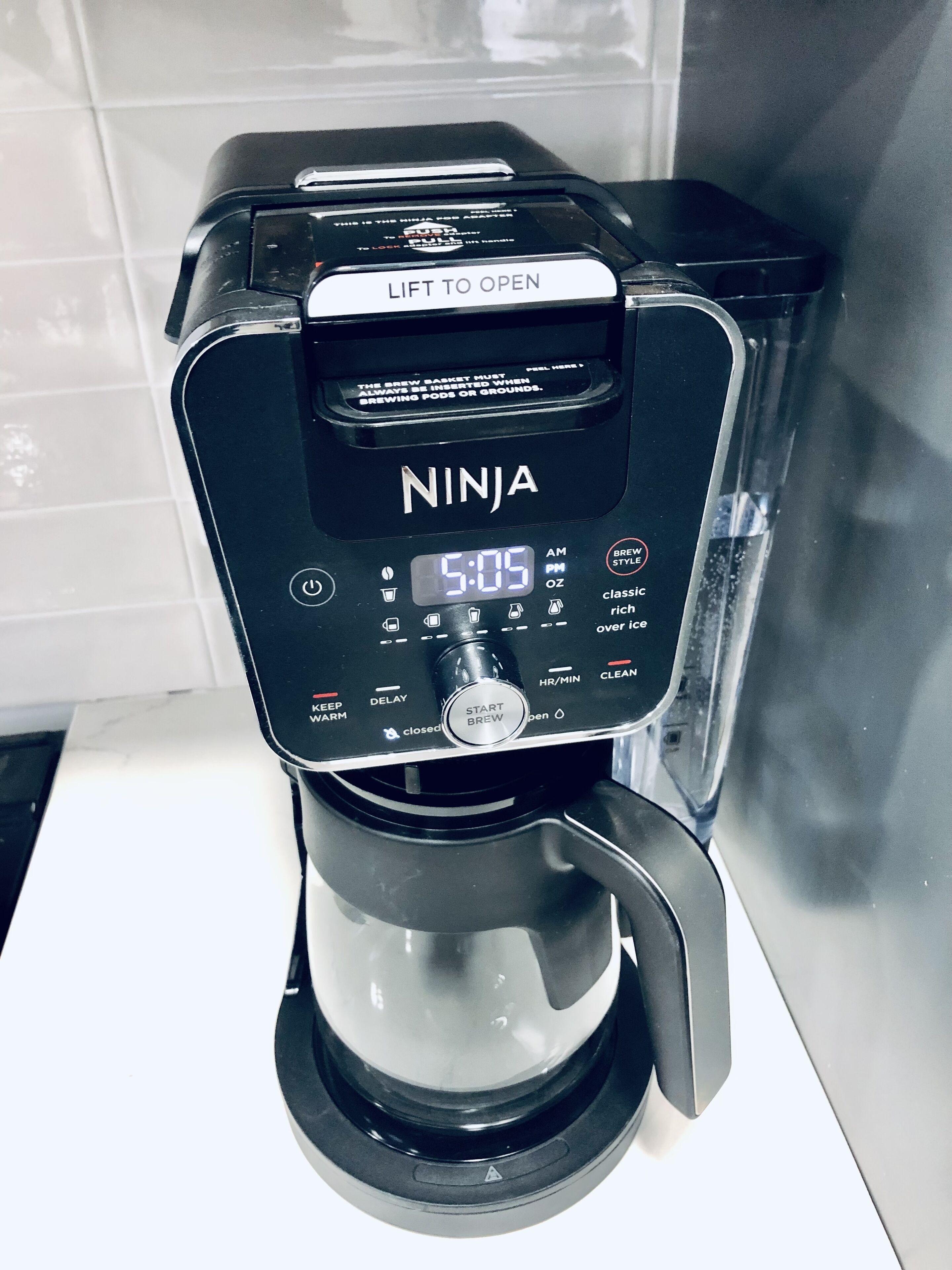 Una màquina de cafè Ninja amb pantalla digital, un mecanisme d'obertura elevable i una olla per a fer el cafè.