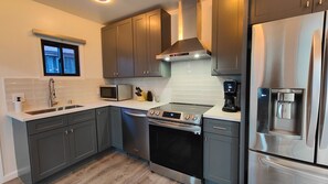 A modern kitchen with grey cabinets, a stainless steel refrigerator, a built-in oven, and a microwave.
