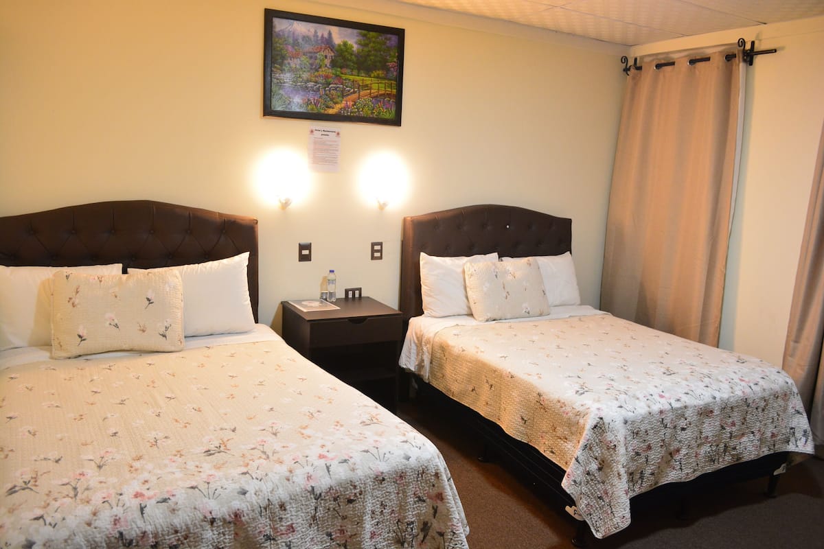 A hotel room with two beds, a nightstand, a lamp, and a painting on the wall.