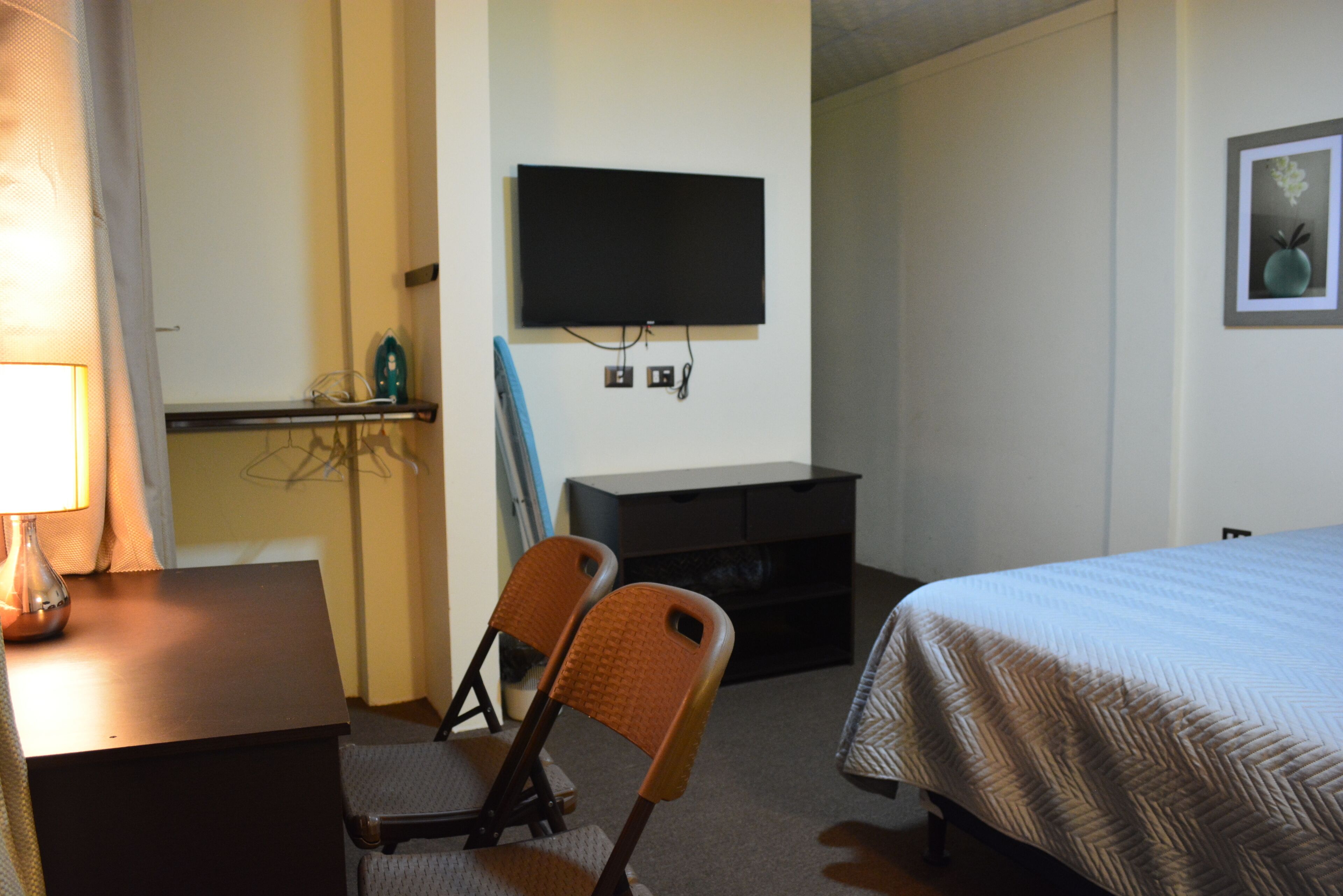 Een hotelkamer met een bed, een bureau met een lamp, een stoel, een aan de muur bevestigde televisie en een schilderij.