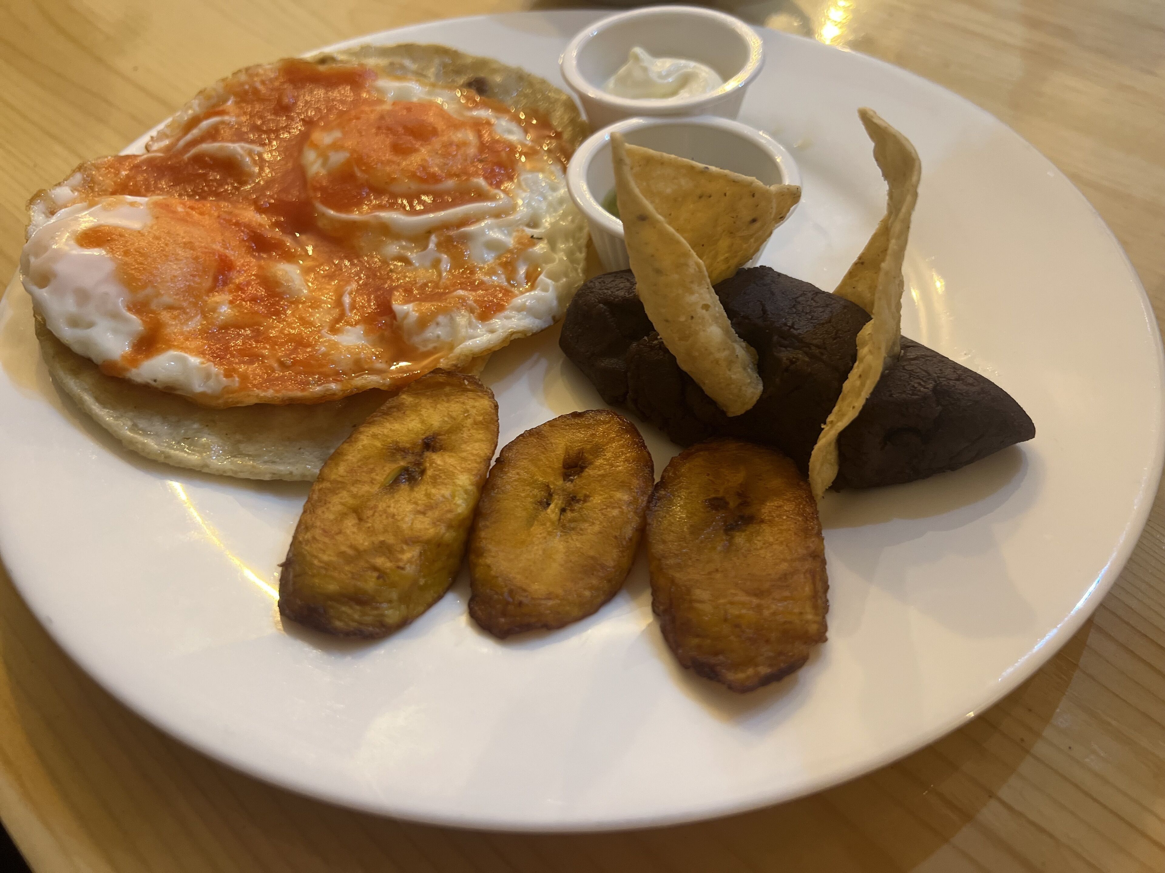 Un plato con un huevo frito, plátanos fritos, rodajas de plátano frito y un trozo de plátano frito.