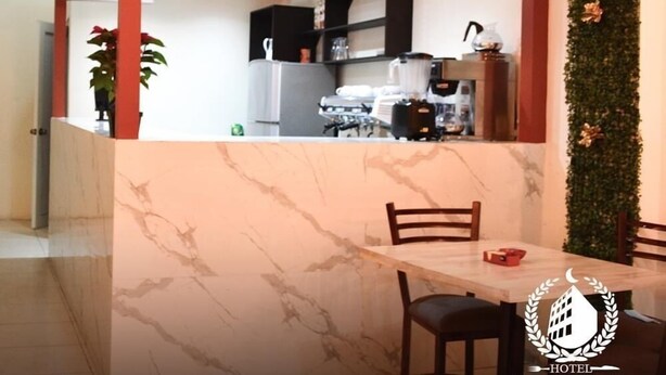 A cafe area with a marble table and chairs, a reception desk, and a kitchen visible through the partition. - Hotel y Restaurante Premier  (La Esperanza)
