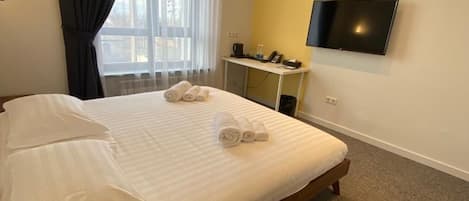 A hotel room with a bed, a desk, a flat-screen TV, and a window with curtains.