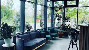 A modern interior with large windows, a blue sofa, and potted plants. - Hotel 78 Cafe (Karakol)