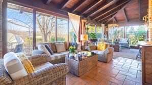 Un espacio habitable acogedor y de concepto abierto con muebles de mimbre, una mesa de centro con vajillas y ventanas amplias que ofrecen vistas al exterior.