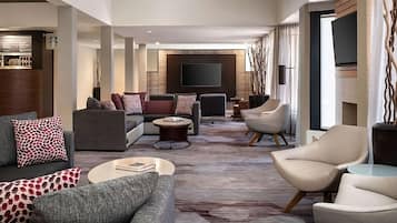 A modern living room with a sectional sofa, armchairs, a coffee table, and a flat-screen TV mounted on the wall.