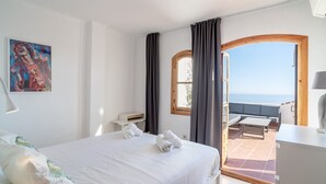 Un dormitorio con cama, un cuadro, una ventana con cortinas y vista al mar.