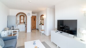 Una sala de estar moderna con sofá, mesa de centro, televisión y una cocina al fondo.