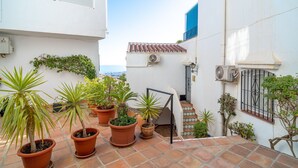 Un estrecho patio con baldosas de terracota, plantas en macetas y una escalera que sube a un nivel superior.