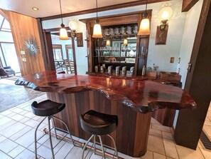 A bar area with stools, a wooden counter, and hanging pendant lights.