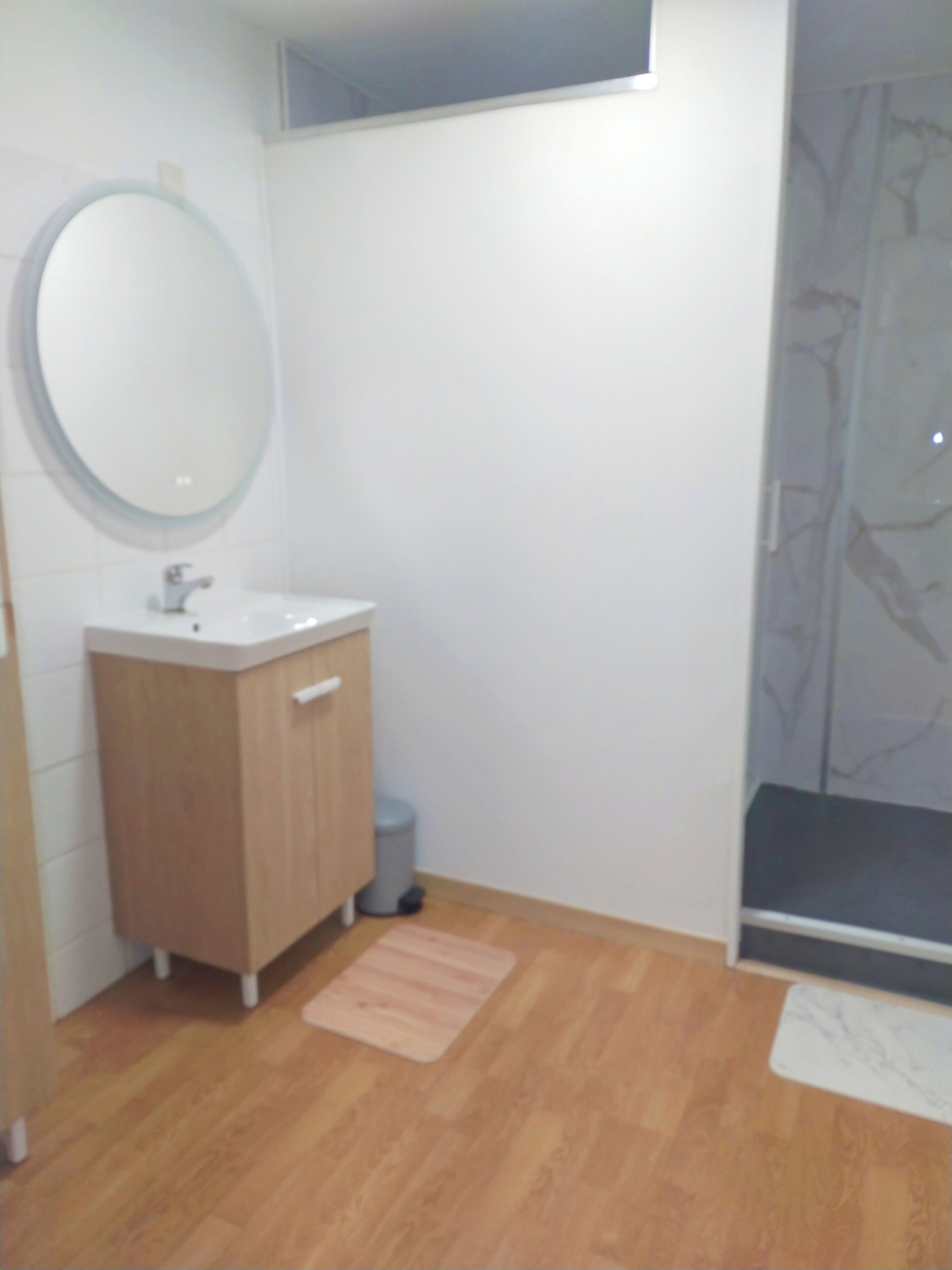 Une salle de bain avec un meuble en bois, un miroir rond et un espace douche.