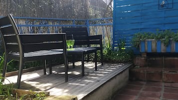 En patio med to sorte metalbænke og et bord, omgivet af et blåt hegn og et bambushegn.
