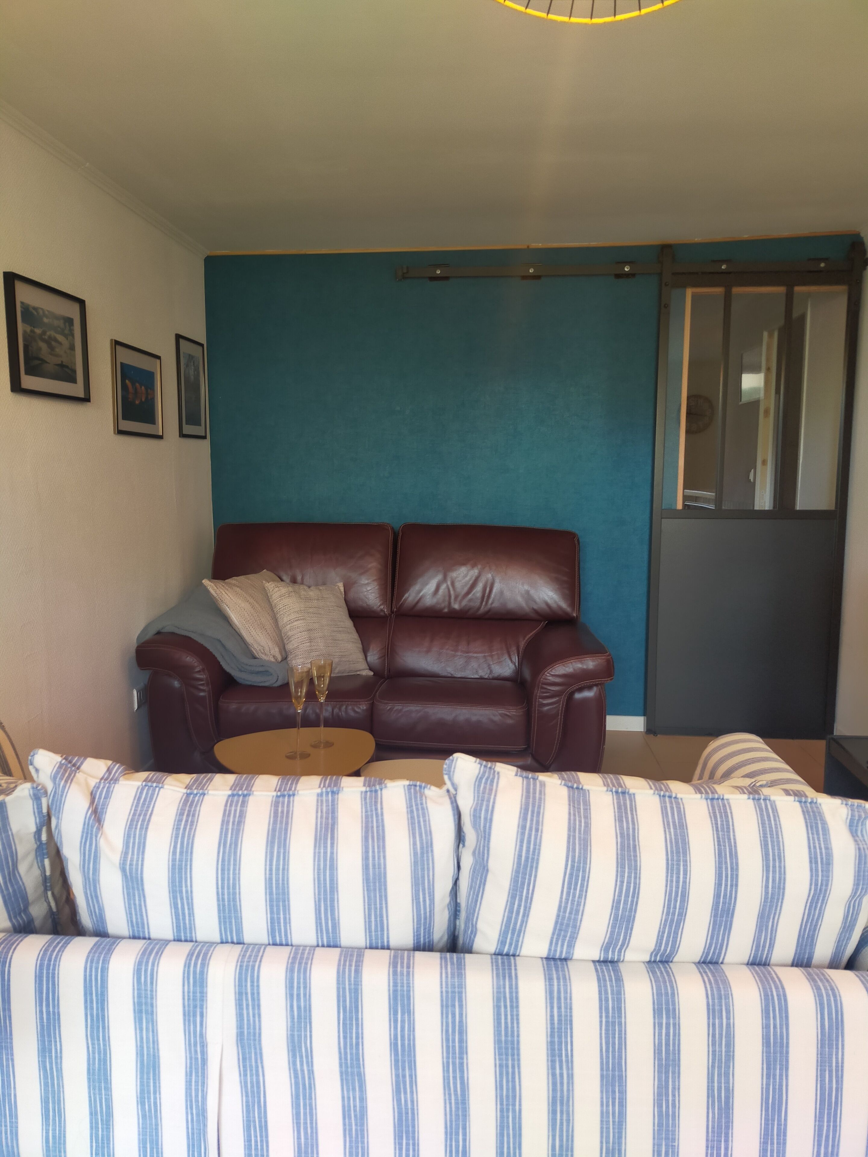 En stue med en brun lædersofa, en stribet sofa og et rundt bord med to glas.