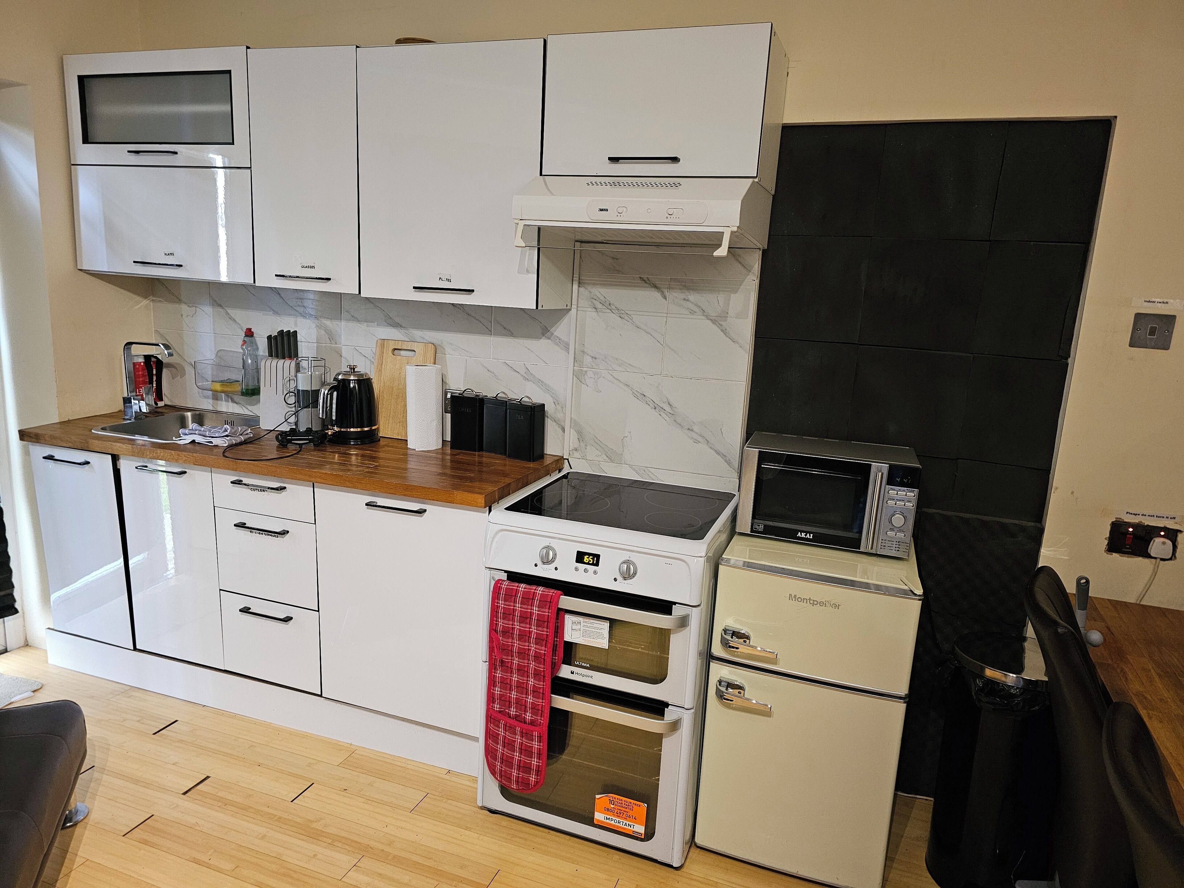 A compact kitchen with white appliances, a wooden countertop, and a black backsplash.