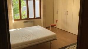 Un dormitorio con cama, ventana, radiador, una silla y armario.