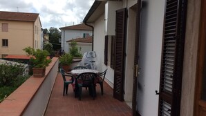 Un estrecho pasillo exterior con suelo de baldosas, una mesa con sillas y una parrilla cubierta.