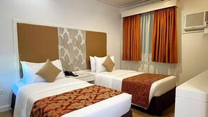 A hotel room with two beds, a large window with orange curtains, and a built-in air conditioning unit. - La Piazza Hotel and Convention Center  (Legazpi)