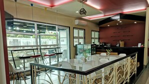 A modern restaurant with a bar area, large windows, and a view of the outdoors. - La Piazza Hotel and Convention Center  (Legazpi)