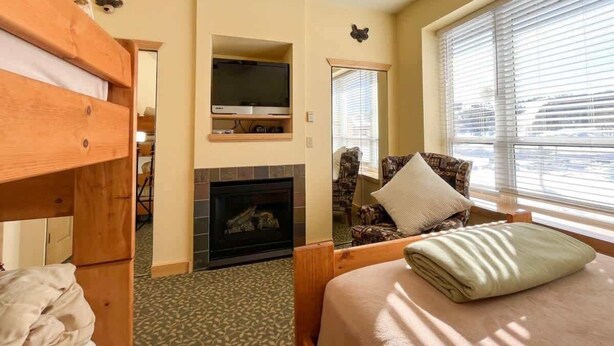 A cozy room with a bunk bed, a fireplace, a television, and a window with blinds. - 1BR,1BA for 5 – Close to Outdoor Activities (Brian Head)