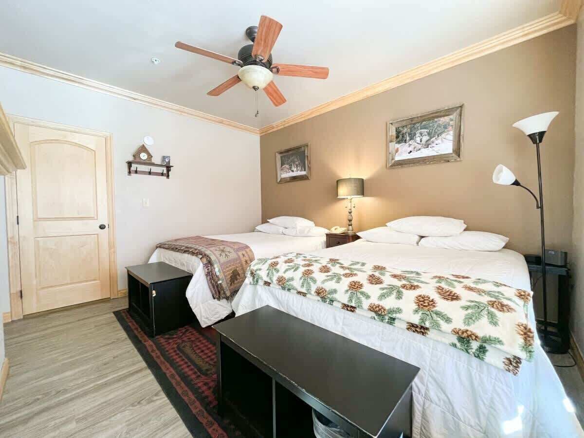 A bedroom with two beds, a ceiling fan, bedside lamps, and a door.