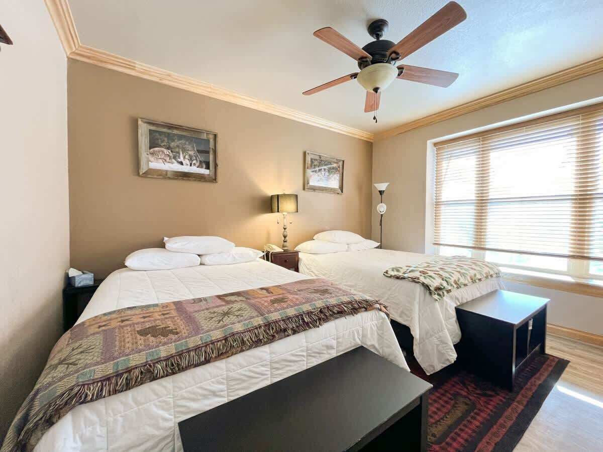 A bedroom with two beds, a ceiling fan, and a window with blinds.