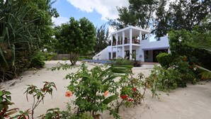 A white building with a balcony, surrounded by greenery and a sandy area. - Kivuli Beach Resort Paje (Paje)