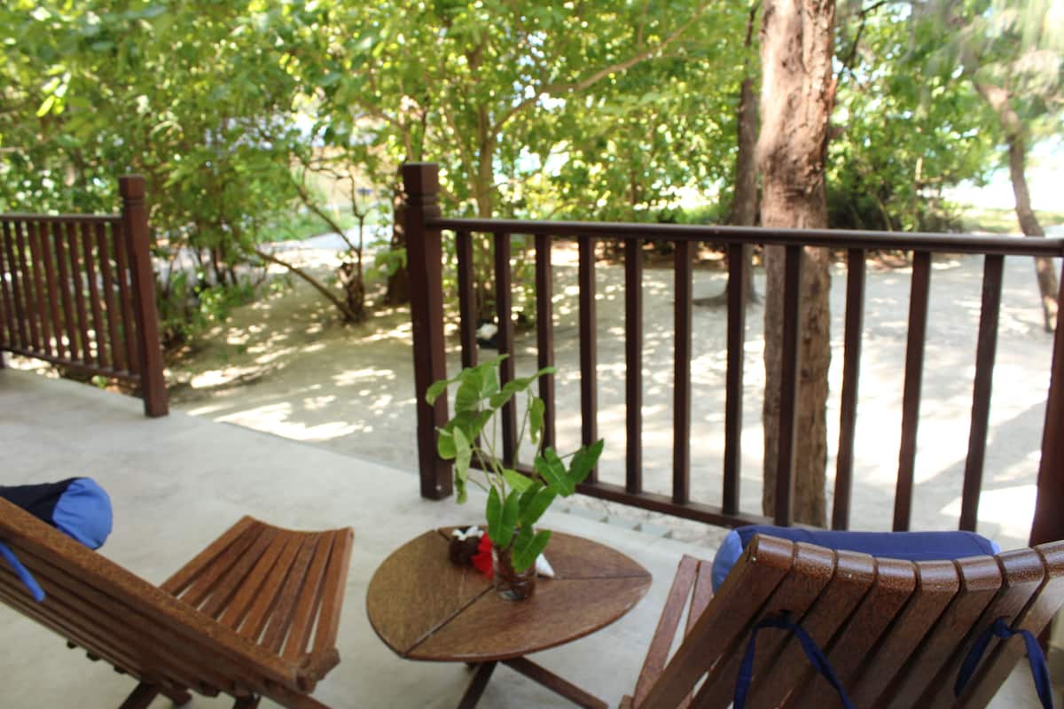 Una terraza de madera con dos sillones y una pequeña mesa, rodeada de árboles.