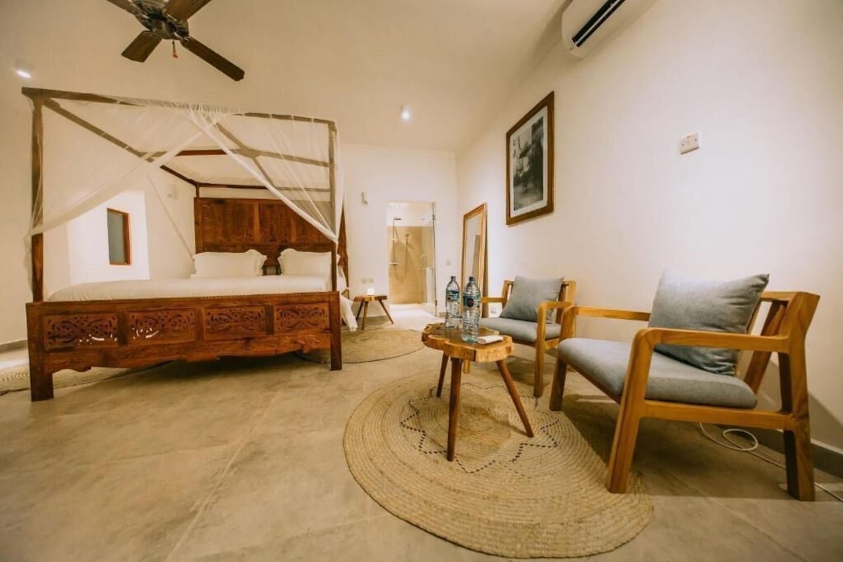 A bedroom with a four-poster bed, a wooden chair, a small round table, and a ceiling fan.