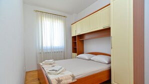 A compact bedroom with a wooden bed, a built-in wardrobe, and a window with sheer curtains. - Apartment 2224/67734 (Istria - Rovinj), 800m from the beach (Rovinj)