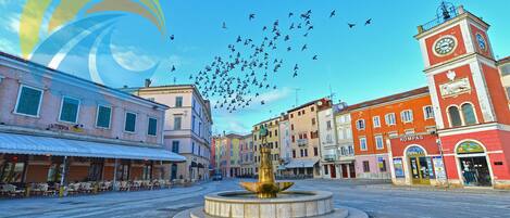 A public square with a fountain, surrounded by historic buildings with shops and a clock tower.