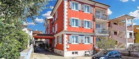 Un edificio de varios pisos con balcones, un coche estacionado frente a él y un cielo despejado.