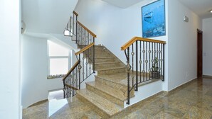 A staircase with a wooden handrail and black metal balusters, leading to a landing with a large poster and a potted plant.