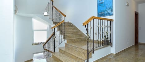 A staircase with a wooden handrail and black metal balusters, leading to a landing with a large poster and a potted plant.